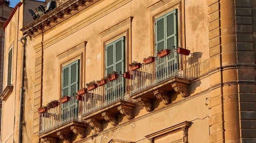 Detail of the façade of a historic building in warm sunlight with balconies, Ortigia Island, Isola