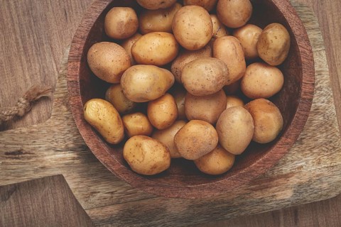 A bowl filled with small, freshly harvested potatoes sits on a rustic wooden cutting board,