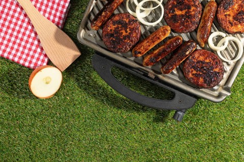 Barbecue with sausages and burgers next to a red and white chequered cloth on a green lawn
