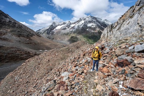 Mountaineer on hiking trail in steep rocky mountain landscape with fresh snow in summer, behind