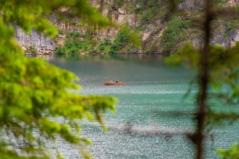 A small boat on a spacious, quiet lake surrounded by lush trees, Pragser Wildsee, South Tyrol,