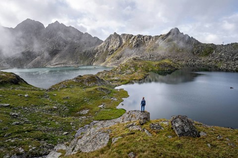 Mountaineer on a rock in front of mountain lakes Wangenitzsee and Kreuzsee, cloudy mountain peaks