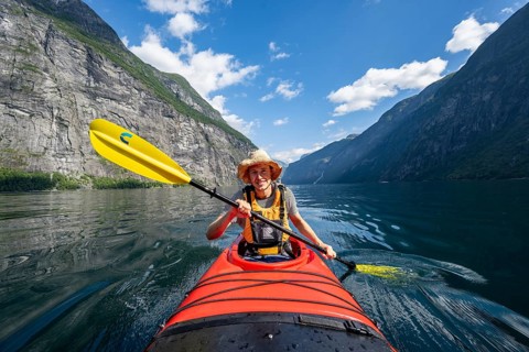 Kayak trip on the Geirangerfjord, young man paddling in red kayak, atmospheric fjord landscape,