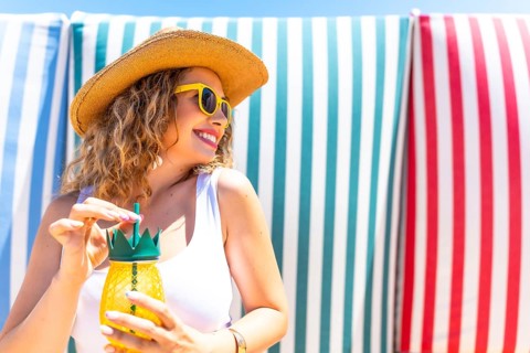 Young woman with straw hat and sunglasses enjoying a refreshing pineapple cocktail on a beach with