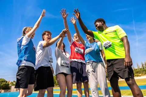 Group of young athletes celebrating their victory on a running track, raising hands together in a