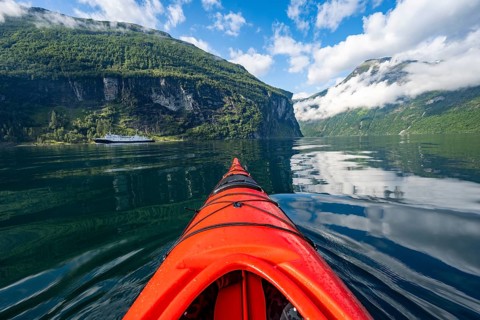 Kayak trip on the Geirangerfjord, tip of a red kayak in the fjord with reflection, atmospheric