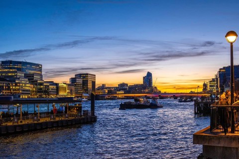 Tugboats sailing on thames during sunset with london's illuminated skyline reflecting on the water