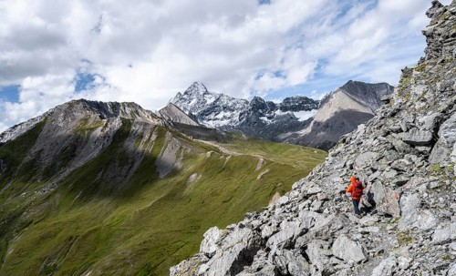 Mountaineer on steep rocky hiking trail, descent from the summit of Kastenegg, view of picturesque