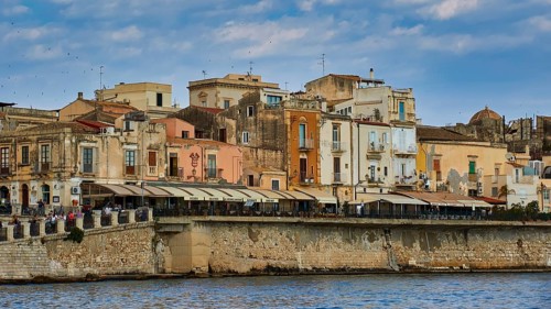 Coastal view with a mix of old buildings and modern terraces along the waterfront, boat trip around