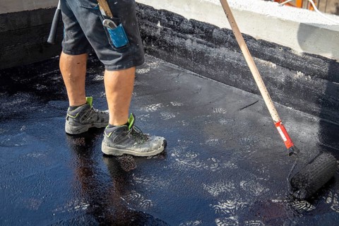 Flat roof waterproofing: Roofer applying the bitumen primer