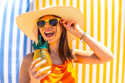 Young woman with sunglasses and a straw hat, enjoying a tropical pineapple juice on a colorful