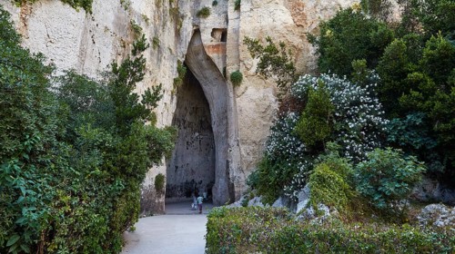 Cave Ear of Dionysus, Overgrown cave entrance with lush vegetation and rocks, people in the