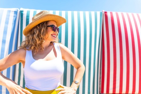 Young woman with curly hair, sunglasses, and straw hat posing with hands on hips in front of