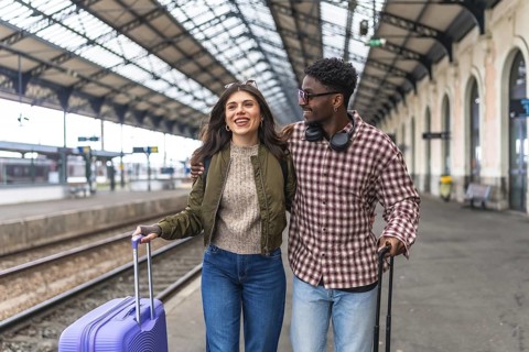 Young multi ethnic couple walking together with luggage at a train station platform, enjoying their
