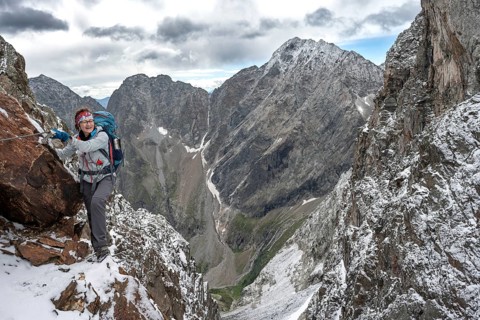 Female mountaineer on a rope-secured climb in a steep rocky mountain landscape with fresh snow in