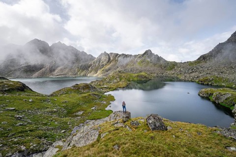 Mountaineer on a rock in front of mountain lakes Wangenitzsee and Kreuzsee, cloudy mountain peaks