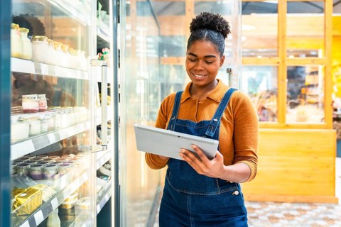 Young supermarket employee using digital tablet checking inventory of dairy products inside of a