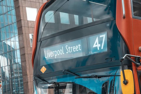 Red double decker bus number 47 showing liverpool street destination, reflecting modern buildings