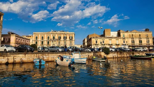 Boats on a waterfront in a town in the warm light and under a blue sky, boat trip around the island