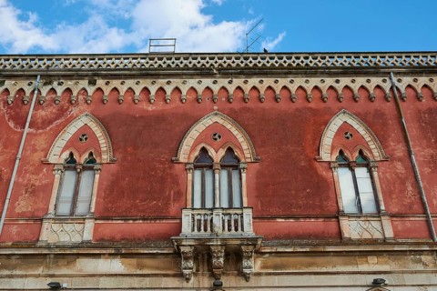 Red façade of a building with Gothic windows and decorative details, Ortigia Island, Isola di