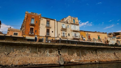 Houses with different facades on a stone coastal wall under a sunny sky, boat trip around the