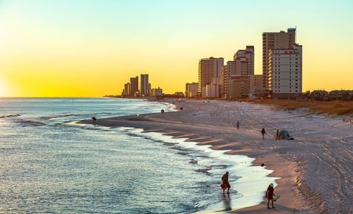 People walking and playing on the beach as the sun sets over the Gulf of Mexico at Gulf Shores,