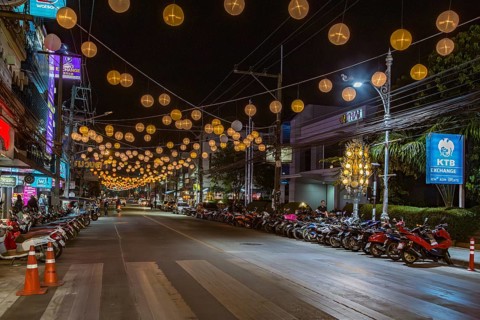 Scooters and motorcycles under lighted spheres strung across downtown street in Chiang Rai,