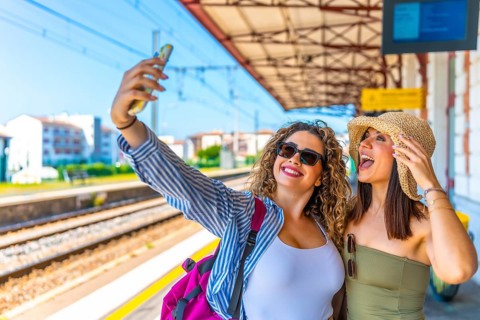 Two happy female tourists taking a selfie with a smartphone at a train station before departure