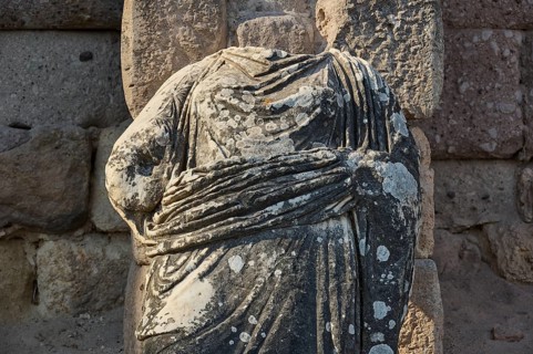 Close-up of a headless stone statue in a landscape of ruins, torso of a statue of a god, Asklipion,