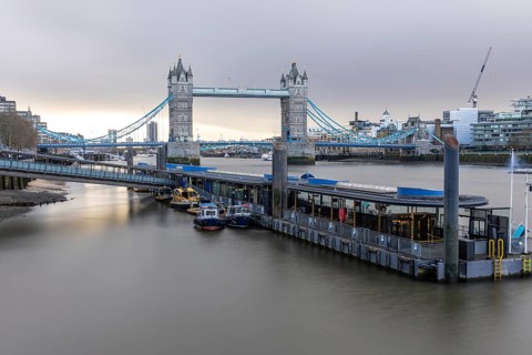 Tower bridge standing majestically over the river thames with boats moored at a pier, showcasing