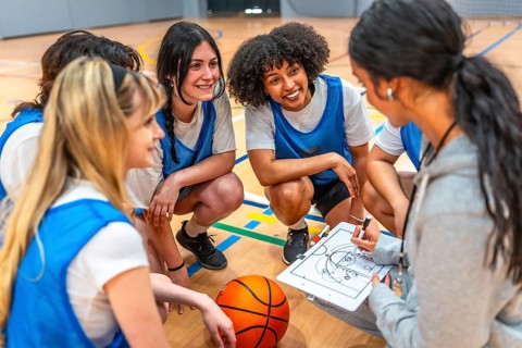 Female basketball coach drawing a play on a clipboard while explaining game strategy to her young