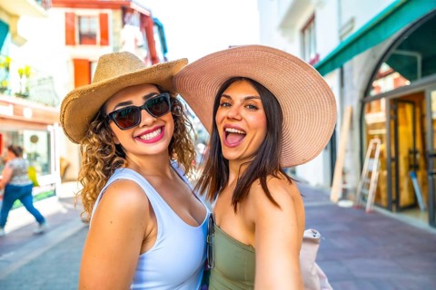 Two female tourists are taking a selfie while walking down a city street during their summer