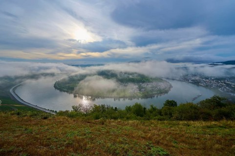 Fog-covered river landscape with rolling hills and overcast sky in calm light, summer, Rhine bend