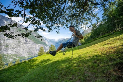 Young man swinging, Blomberg Gård, above the Geirangerfjord, view of idyllic fjord landscape, near