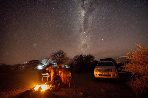 Tourists sitting around a campfire next to their off-road vehicle at night, night shot with starry
