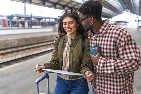 Happy tourists consulting map at train station while waiting for train, planning their next