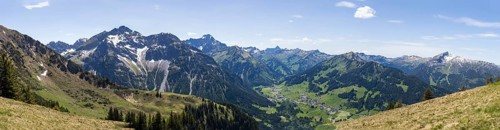 Sweeping panorama of the Alps with snow-capped mountains and green valleys under a blue sky with a