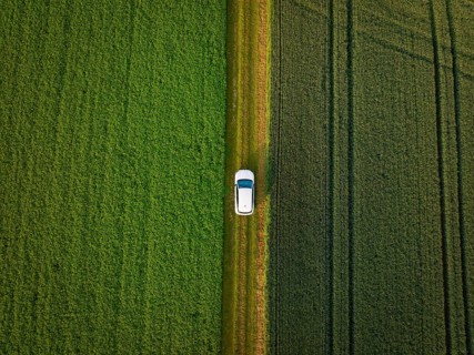 Car on a narrow path between two neighbouring green fields from the air, Deer E- CarSharing,