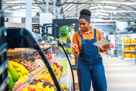 Young supermarket employee using a digital tablet and checking fresh products in a refrigerated