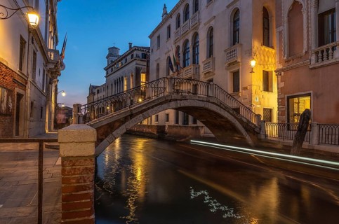 Small pedestrian bridge arching over canal in venice, italy at twilight with light trails