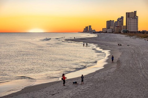 People walking and playing on the beach as the sun sets over the Gulf of Mexico at Gulf Shores,