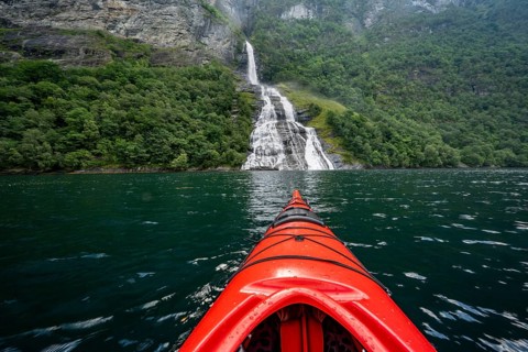 Kayak trip on the Geirangerfjord at the Freier waterfall, tip of a red kayak in the fjord,