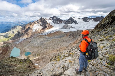 Mountaineer with helmet in high mountain landscape, view of blue glacier lakes, mountain peaks