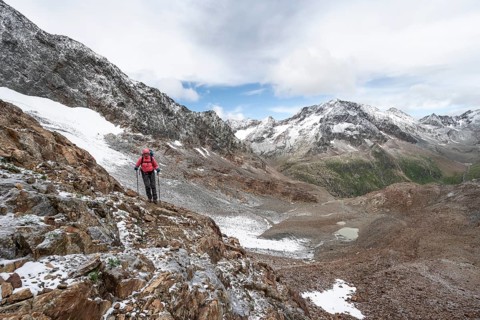 Mountaineer on a rocky hiking trail in a steep rocky mountain landscape with fresh snow in summer,