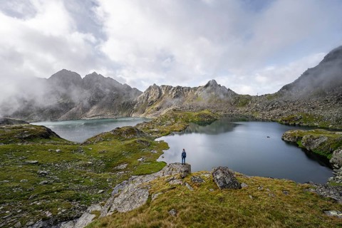 Mountaineer on a rock in front of mountain lakes Wangenitzsee and Kreuzsee, cloudy mountain peaks