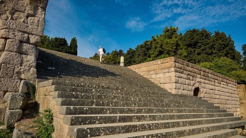 Stone staircase leads to a ruin surrounded by trees, a person climbs the steps, open staircase to