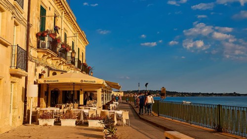 Cosy restaurant on a promenade with sea view. People walking in sunny weather, Ortigia Island,