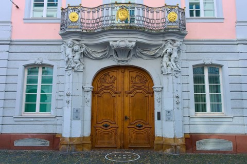 Magnificent wooden door of a pink façade with classical sculptures and decorative details in