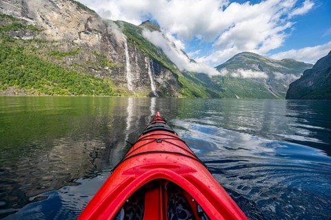 Kayak trip on the Geirangerfjord with waterfall The Seven Sisters, tip of a red kayak in the fjord,