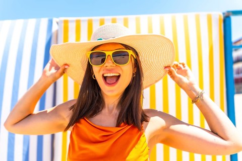 Young woman wearing a straw hat and sunglasses, smiling brightly while enjoying the summer sun,